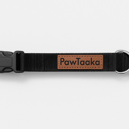 Flat lay of PawTaaka Basics Solid Strap Collar – Midnight Black featuring black nylon strap, metal D-ring, and PawTaaka leather logo patch.